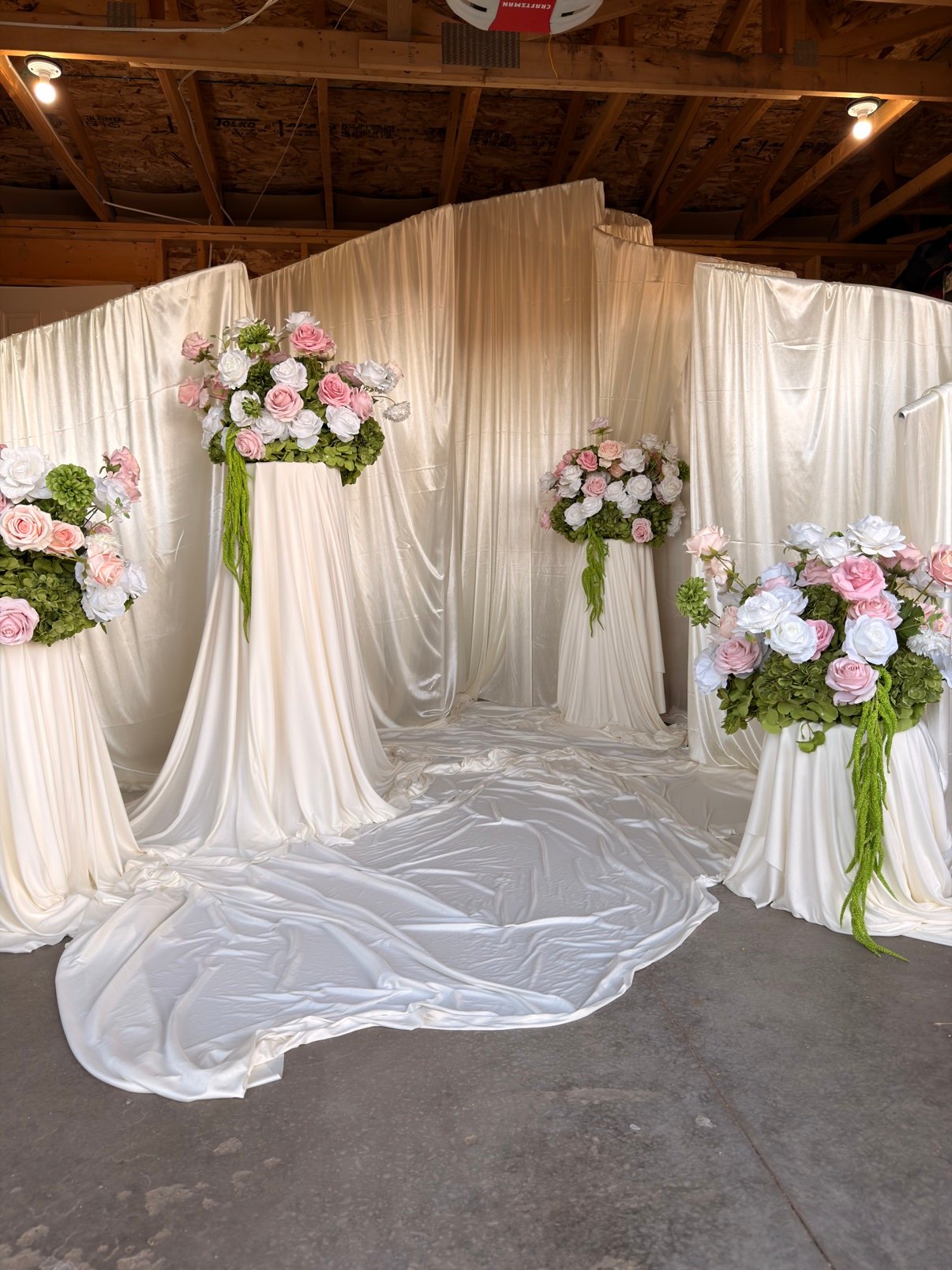 White draped ceremony backdrop with floral arrangements by Penbaga Events