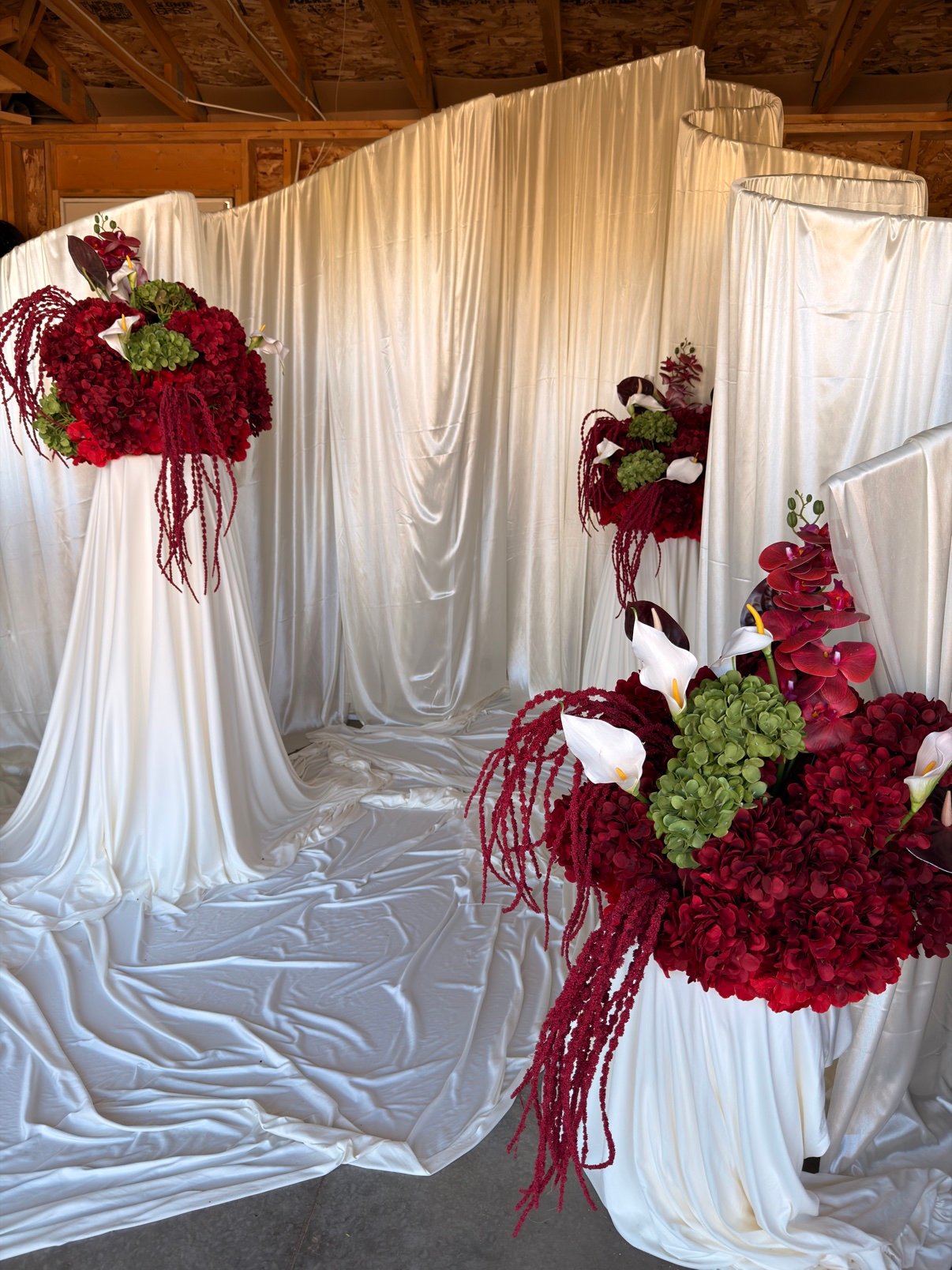 Burgundy draped backdrop with floral arrangements by Penbaga Events